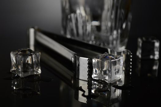 A closeup of some ice cubes and a set of tongs for adding some into a glass.