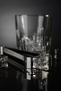 A closeup of some ice cubes and a set of tongs for adding some into a glass.