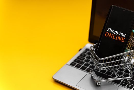 Shopping cart with smartphone on notebook. Online shopping concept.