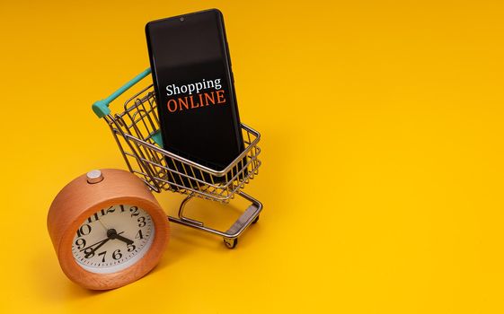 Shopping cart with smartphone and clock. Online shopping concept.