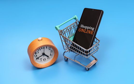 Shopping cart with smartphone and clock. Online shopping concept.
