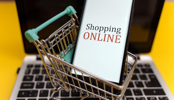 Shopping cart with smartphone on notebook. Online shopping concept.