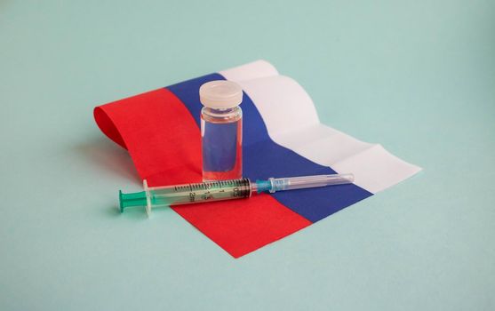 The vaccine and the injection syringe are on the small flag of Russia. For the prevention, immunization and treatment of coronavirus infection. The concept of medicine and healthcare.