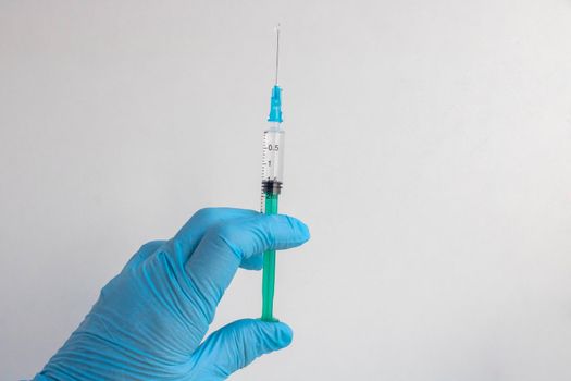 A blue-gloved hand holds a syringe. A syringe with a sharp needle in the hand. The concept of medical treatment. Laboratory background. The concept of vaccination. Space for text, the concept of health insurance
