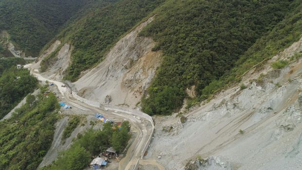Construction of protective barriers against rock falls and landslides in the mountainous province. Aerial view of heavy machinery on the construction of a mountain road. Cement block road protection from landslides. Philippines, Luzon, North Batad.
