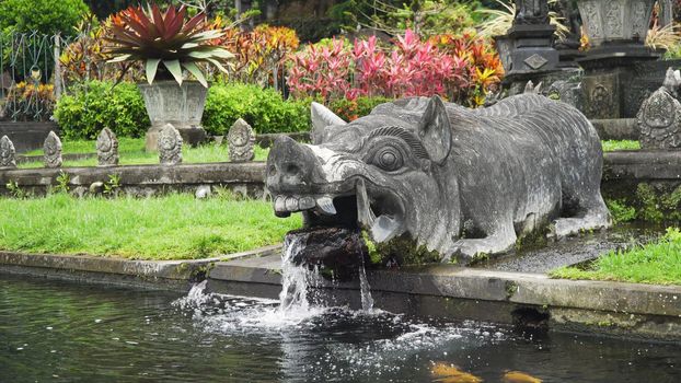Hindu Balinese Water Palace Tirta Gangga with statues of the gods, fountains in the form of a wild boar on Bali island, Indonesia. Tirta Gangga the former royal water palace is a maze of pools and fountains surrounded by a lush garden and stone carvings and statues.