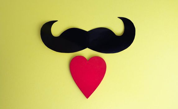 Father's Day concept. Black mustache and red heart on a yellow paper background.