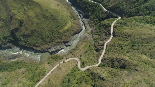Aerial view of mountain river in the cordillera, road on the slopes, mountains covered forest, trees. Cordillera region. Luzon, Philippines.