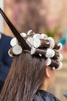 Hair curlers are wound on the head of a young girl in a beauty salon. Close-up