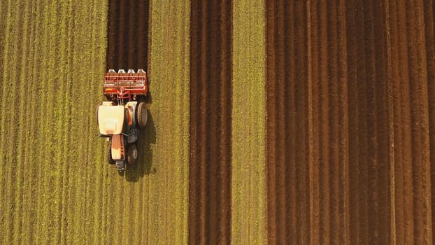 Farmer in tractor preparing land with seedbed cultivator in farmlands. Tractor plows a field. Agricultural work in processing, cultivation of land. Farmers preparing land and fertilizing. Agricultural workers with tractors.