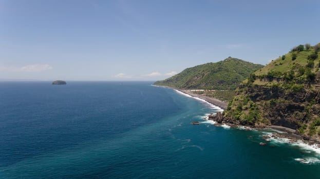 Rocky coast with high cliffs, sea coast, ocean, mountains, sea, beach, sky, clouds. Bali, sea surf with breaking waves on the coast, Indonesia. Ocean with waves and rocky cliff.