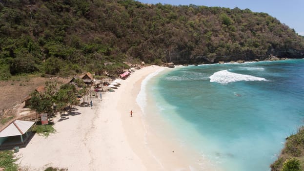 Aerial view of beautiful white sand Atuh beach for relax. Clear blue ocean waves rolling to the beach. Nusa Penida, Bali, Indonesia. Travel concept.