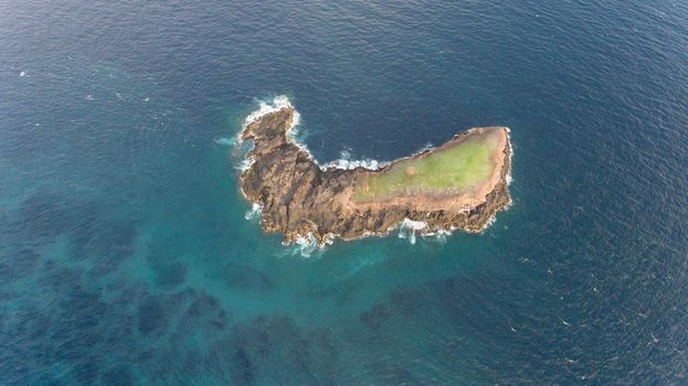 Tropical rocky island in the sea. Aerial view tropical island among the ocean. Waves break on the shore of the island Travel concept.