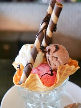 Mixed ice cream scoops in wafer bowl. Dessert Sundae with Neapolitan Flavors of Ice Cream - Glass Dish with Scoops of Chocolate, Vanilla, and Strawberry Ice Cream with Rolled Cookie Biscuits and Garnishes