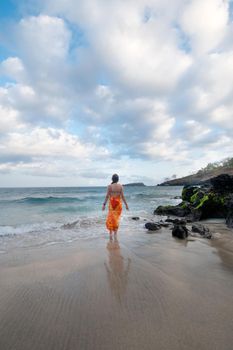 Girl standing on sandy beach among the waves and looks at the sea.Young girl relaxing at Tropical Beach. Recreation and pampering on the seashore in summer and sunny day.