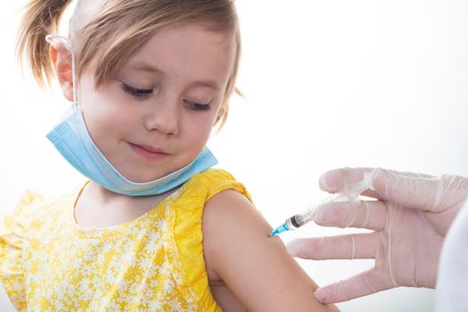 Doctor in a white coat is vaccinating a young Caucasian girl in yellow dress isolated on white background