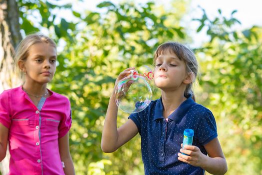 A girl blows bubbles, another girl watches her closely