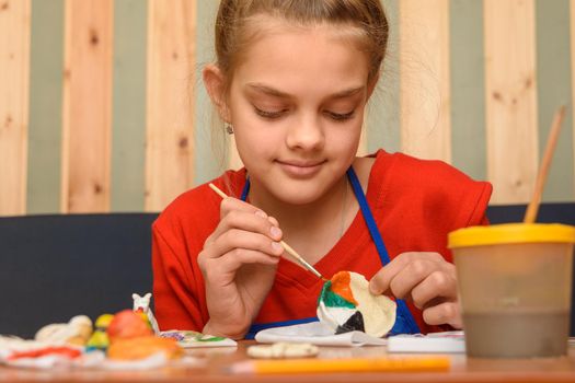 A girl paints a craft from salt dough with watercolors