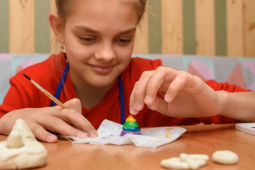 Girl rejoices painting a figurine made of salt dough