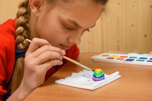 A girl carefully paints a figurine made of salt dough