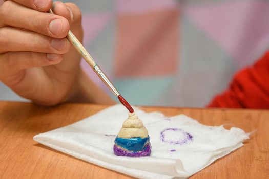 A girl paints a pyramid of salt dough with different colors, close-up