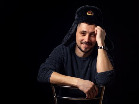 Portrait of a smiling man of thirty years of Caucasian appearance in a Soviet officer's fur hat on a black background