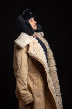 Portrait of a Caucasian-looking man in a Soviet officer's fur hat and an army sheepskin coat, standing at attention