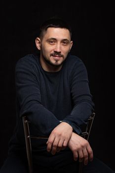 Portrait of a smiling man of thirty years of Caucasian appearance in a regular sweater on a black background