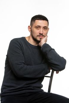 Portrait of an ordinary man in a dark plain sweater sitting on a high-backed chair