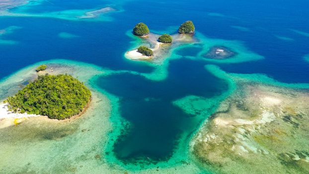 Small Island with beautiful beach, palm trees by turquoise water view from above. Britania Islands, Surigao del Sur, Philippines.