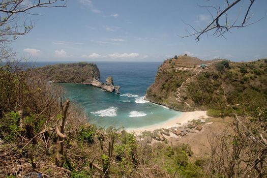 Beach with with azure water, rocky mountains and clear water at sunny day. Clear blue ocean waves rolling to the beach. Nusa Penida, Bali, Indonesia. Travel concept.
