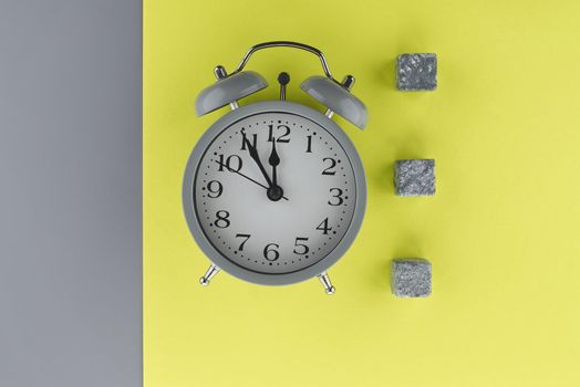 Alarm clock on a two tone grey and yellow background with copy space viewed as a flat lay. Renovation and color trends concept