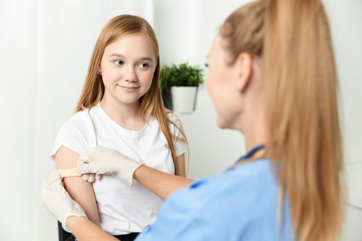 a female doctor next to a girl seals her arm with a plaster. High quality photo