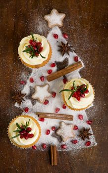 Christmas cupcakes with vanilla frosting, cranberries and rosemary on wooden background