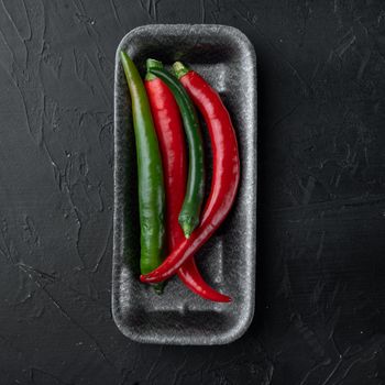 Ripe Red and green chili pepper set, in plastic tray, on black background, top view flat lay