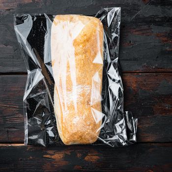 Ciabatta panini bread in a plastic bag, on dark wooden background, top view flat lay