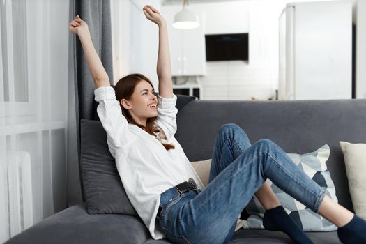 woman sitting with raised hands up verse on the couch free time apartment. High quality photo