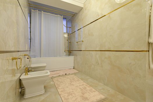 Modern luxury beige and golden bathroom with toilet, bidet and bathtub