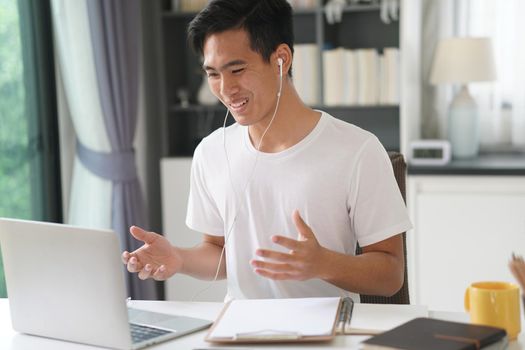 asian young teenage student man entrepreneur wear earphones working by video call conference studying learning online at home. e-learning webinar meeting. social distance in covid pandemic