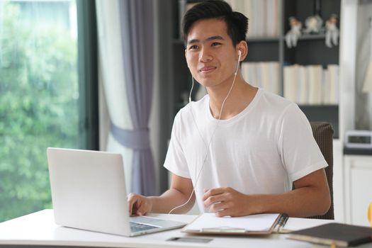 asian young teenage student man entrepreneur wear earphones working by video call conference studying learning online at home. e-learning webinar meeting. social distance in covid pandemic