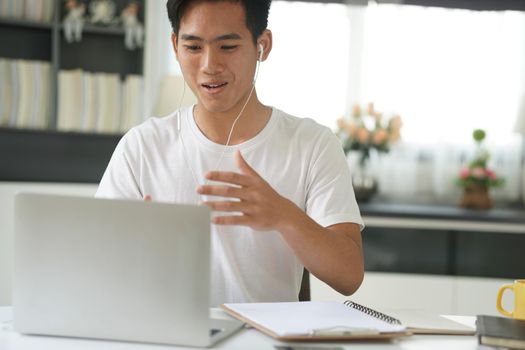 asian young teenage student man entrepreneur wear earphones working by video call conference studying learning online at home. e-learning webinar meeting. social distance in covid pandemic