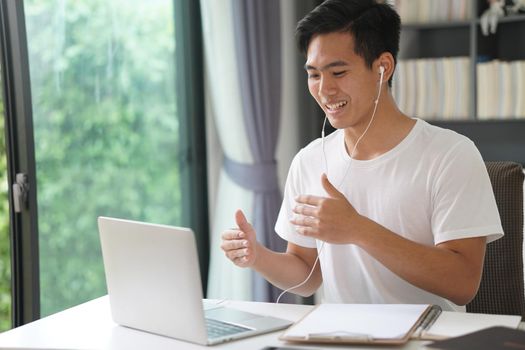 asian young teenage student man entrepreneur wear earphones working by video call conference studying learning online at home. e-learning webinar meeting. social distance in covid pandemic