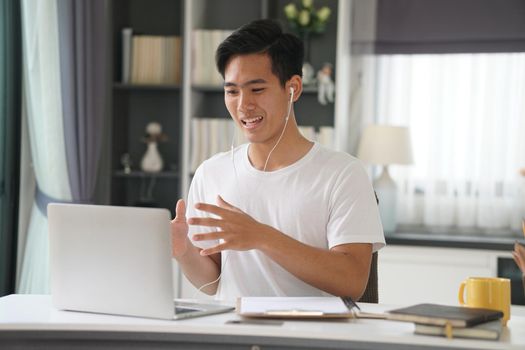 asian young teenage student man entrepreneur wear earphones working by video call conference studying learning online at home. e-learning webinar meeting. social distance in covid pandemic