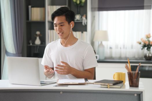 asian young teenage student man entrepreneur wear earphones working by video call conference studying learning online at home. e-learning webinar meeting. social distance in covid pandemic