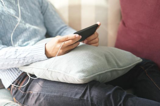 young asian man wearing earphones listening to music on smart phone relaxing on sofa at home
