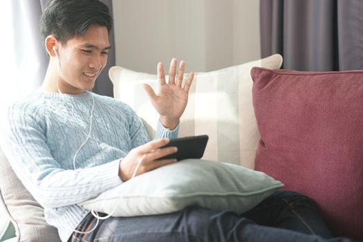 young asian man wearing earphones talking on video call meeting using smart mobile phone
