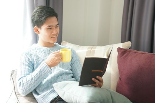 young asian man reading book relaxing on sofa at home. leisure lifestyle