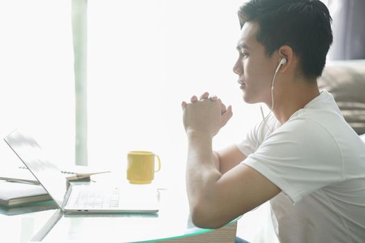asian young student man teenager entrepreneur wear earphones working with computer studying learning online at home. e-learning webinar meeting. social distance in covid pandemic