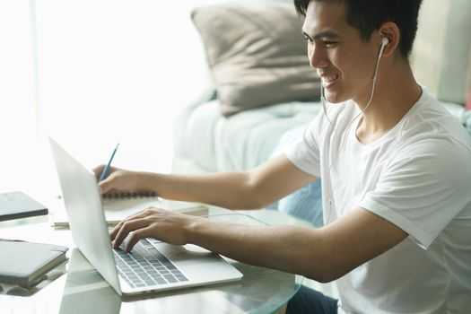asian young student man teenager entrepreneur wear earphones working with computer studying learning online at home. e-learning webinar meeting. social distance in covid pandemic