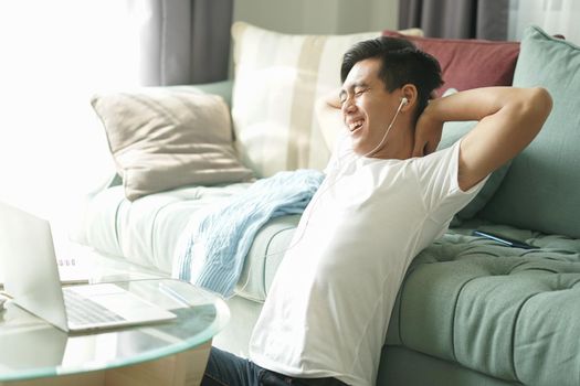 asian young student man teenager entrepreneur wear earphones stretching feeling tired bored sleepy while working with computer studying learning online at home. e-learning education